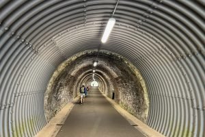 A man walks through the Keswick to Threlkeld Tunnel. In the distance two children are running and scooting out of the tunnel.