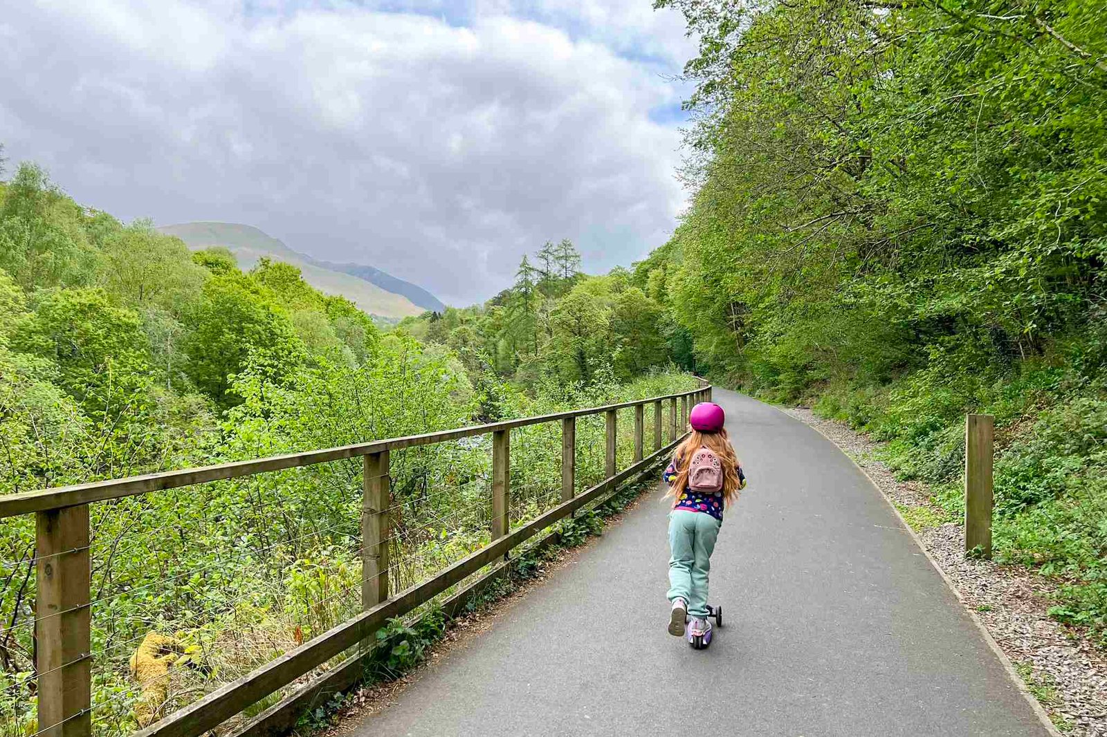 A girl scoots along the Keswick to Threlkeld Railway walk. She is surrounded by trees.