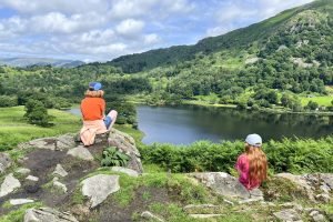 Two children sit on the rocks looking out over Rydal Water from Loughrigg Terrace.